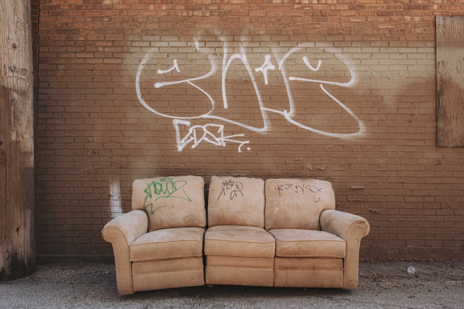 A worn-out sofa sits against a graffiti-covered brick wall in an urban alley.